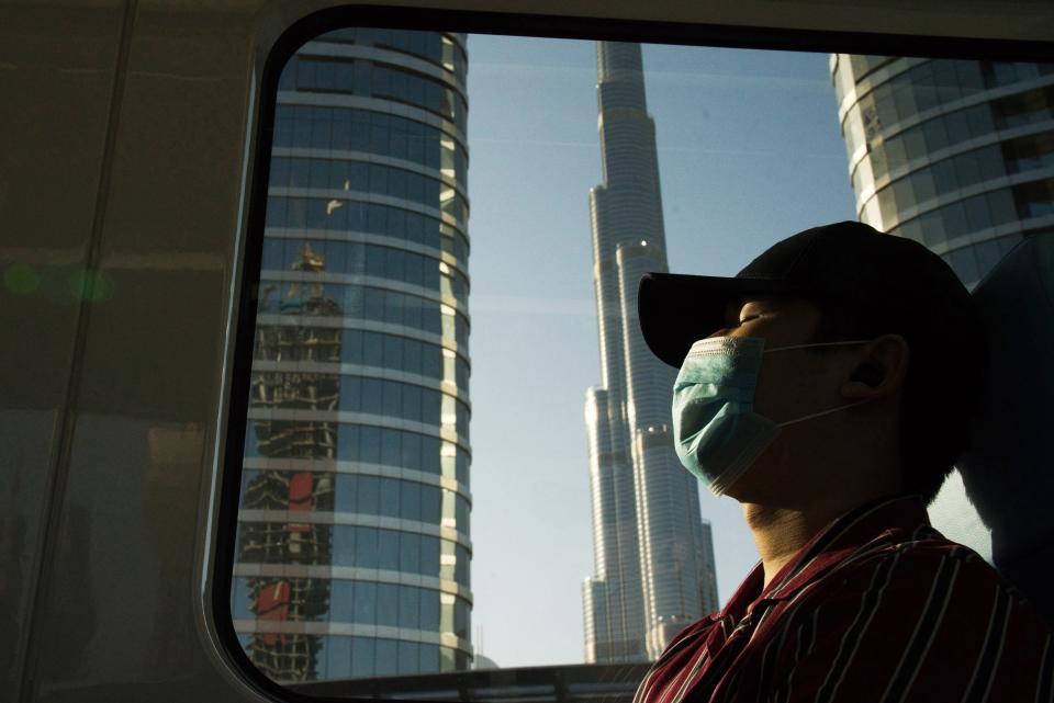 FILE - In this April 26, 2020 file photo, a commuter wearing a face mask to help curb the spread of the coronavirus, sleeps aboard the driverless Metro as it passes the Burj Khalifa, the world's tallest building, in Dubai, United Arab Emirates. After opening itself for New Year’s revelers, Dubai now find itself blamed by countries for spreading the coronavirus abroad. That's as questions swirl about the city-state’s ability to handle reported cases spiking to record levels. (AP Photo/Jon Gambrell, File)