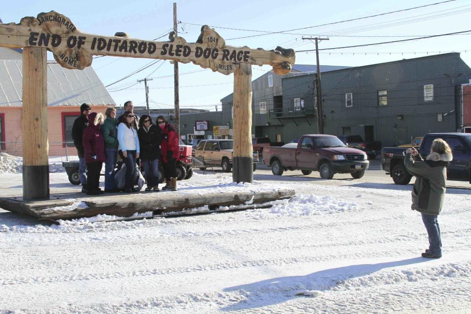 FILE - Tourists pose under the famed burled arch, which serves as the finish line in the nearly thousand-mile Iditarod Trail Sled Dog Race in Nome, Alaska, on Friday, March 7, 2014. Nome Mayor John Handeland said the arch collapsed Saturday, April 27, 2024, likely from wood rot. (AP Photo/Mark Thiessen)