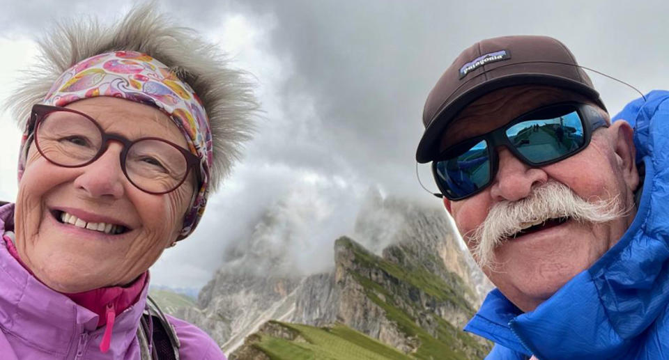 David and Anne are smiling in front of a mountain range. The couple are huge advocates for the budget-friendly approach to travel. 