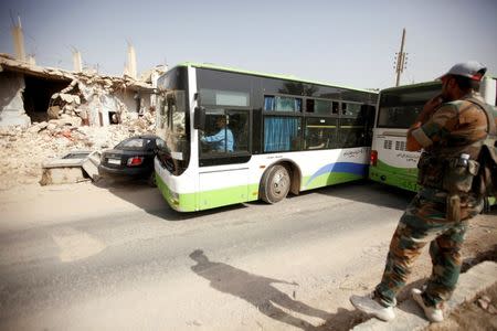 Un soldado del Ejército Sirio vigila mientras personas evacúan en buses el suburbio de Daraya. Residentes y rebeldes comenzaron a abandonar el rodeado suburbio de Daraya en Damasco el viernes, dijeron testigos de Reuters, al comienzo de una operación de evacuación que busca poner fin a una de las confrontaciones más largas en los cinco años que dura la guerra en Siria. REUTERS/Omar Sanadiki