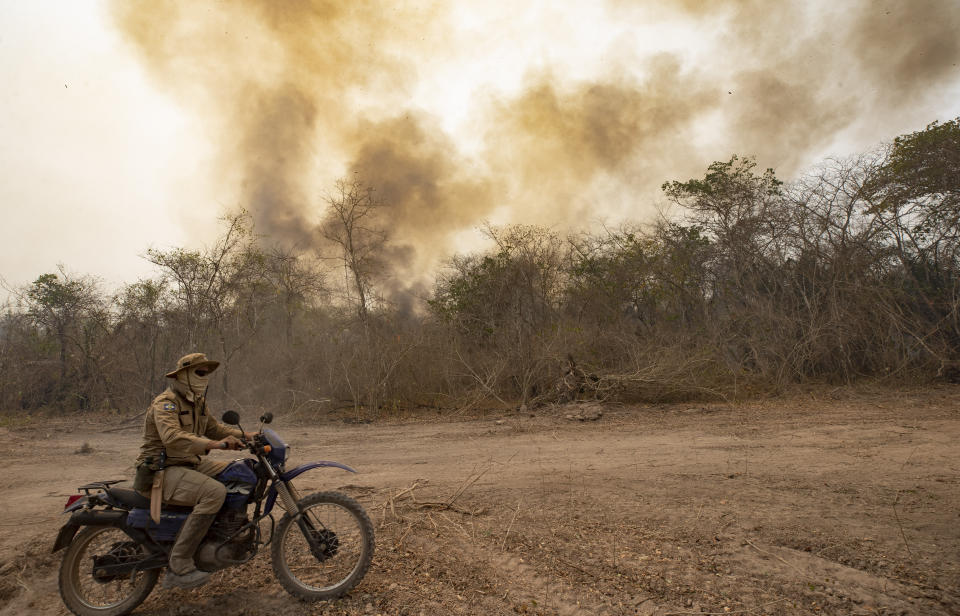 A firefighter rides a motorcycle past a burning area next to the Transpantaneira road at the Pantanal wetlands near Pocone, Mato Grosso state, Brazil, Monday, Sept. 14, 2020. A vast swath of the vital wetlands is burning in Brazil, sweeping across several national parks and obscuring the sun behind dense smoke. (AP Photo/Andre Penner)