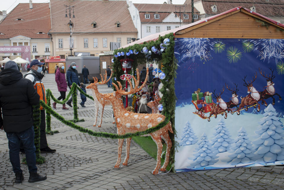 People look at stands in a Christmas market in Sibiu, central Romania, Tuesday, Dec. 28, 2021. As the fast-spreading coronavirus variant omicron rages through Western Europe, officials and experts in low-vaccinated Eastern Europe view it as a forewarning for what much of the region anticipates to be an imminent, post-holiday virus surge.(AP Photo/Stephen McGrath)