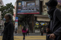 People walk by an outdoor screen displaying a live broadcast of the memorial service for late former Chinese President Jiang Zemin in Hong Kong, Tuesday, Dec. 6, 2022. A formal memorial service was held Tuesday at the Great Hall of the People, the seat of the ceremonial legislature in the center of Beijing. (AP Photo/Vernon Yuen)