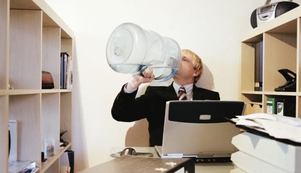 Businessman sitting at desk drinking from water cooler bottle