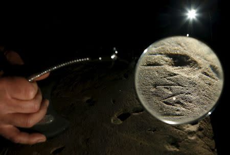 An inscription on an Etruscan stele is seen through a magnifying glass at a restoration centre in Florence, Italy, April 20, 2016. REUTERS/Remo Casilli