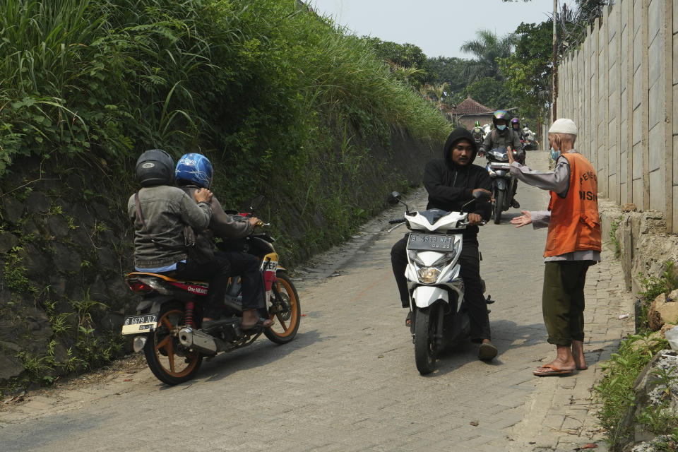 Husin bin Nisan, a volunteer traffic attendant, receives a tip from a motorist in Tangerang, Indonesia, Monday, May 15, 2023. After spending more than three decades picking tips from motorists, the 85-year-old man is finally realizing his dream to go to the Islamic holy cities of Mecca and Medina for Hajj pilgrimage. (AP Photo/Achmad Ibrahim)