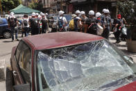 Lebanese youth who volunteered to help clean damaged homes and give other assistance, pass in front of a car that was damaged by last week's explosion, in Beirut, Lebanon, Tuesday, Aug. 11, 2020. The explosion that tore through Beirut left around a quarter of a million people with homes unfit to live in. But there are no collective shelters, or people sleeping in public parks. That’s because in the absence of the state, residents of Beirut opened their homes to relatives, friends and neighbors. (AP Photo/Hussein Malla)