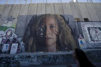 A tourist pauses in front of a mural depicting Palestinian activist Ahed Tamimi on Israel's controversial separation barrier in the West Bank city of Bethlehem, Sunday, June 19, 2022. The summer of 2022 can feel as if the coronavirus pandemic is really over — mask rules and testing requirements are lifting in many countries, including the United States. Full recoveries are generally not expected until at least 2024. (AP Photo/Maya Alleruzzo)