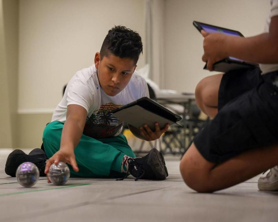 Fourth grader Fernando Gallo, 12, left, places the small robot on the floor while programming it to run a specific pattern as part of the Fab Lab launched at the Phichol Williams Community Center in Homestead, Florida on Wednesday, Jan. 17, 2024.