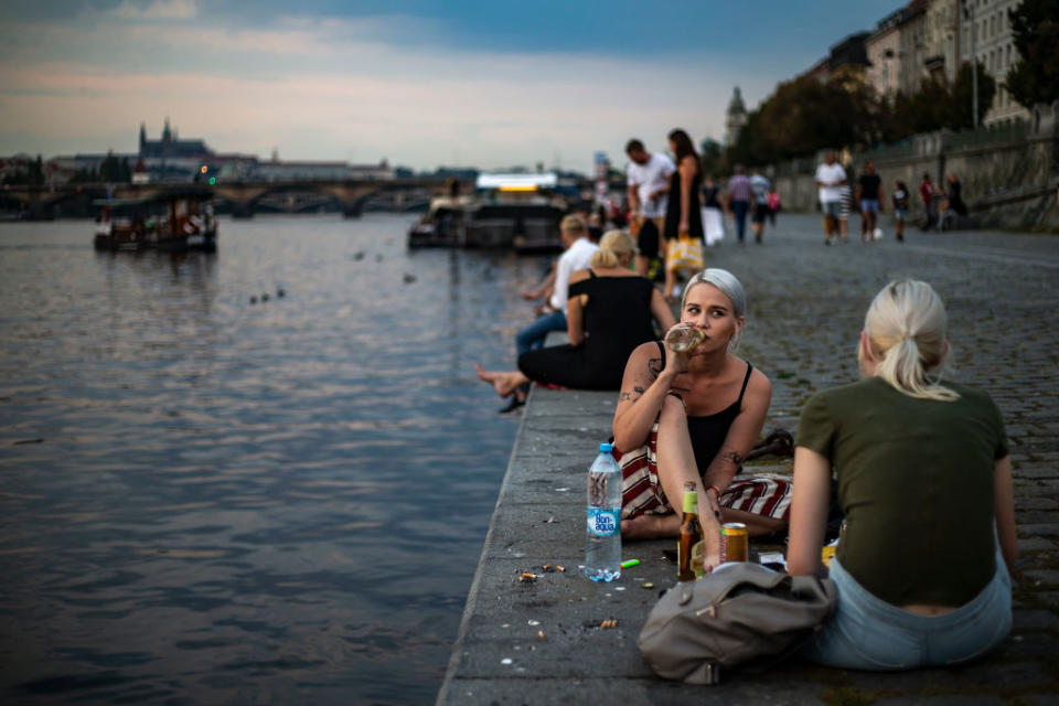 Two woman sitting by the water with a crowd of people in the Czech Republic, which recorded its highest increase of coronavirus cases.