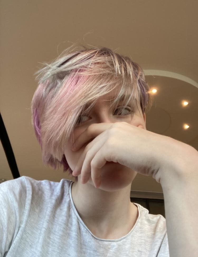 A selfie of Tim. He is covering his face. His hair swoops from the left to the right side of his face. It is dyed pink.