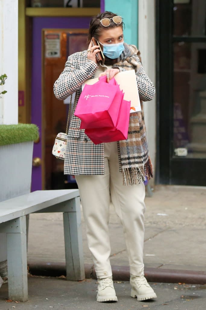 Florence Pugh is seen wearing a plaid jacket and scarf over a cream-colored jumpsuit and a pair of matching boots. - Credit: Splash News