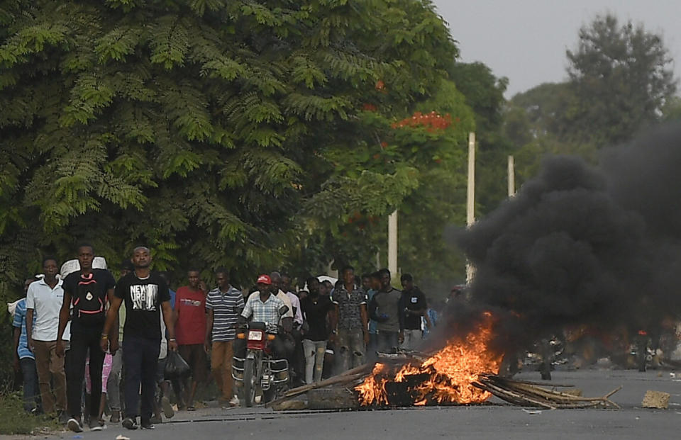 Men walk past a flaming barricade after violence broke out and hundreds of workers fled the area when demonstration near the home town of late President Jovenel Moise grew violent, ahead of his funeral in Quartier Morin, a districto of Cap Haitien, in northern Haiti, Wednesday, July 21, 2021. (AP Photo/Matias Delacroix)