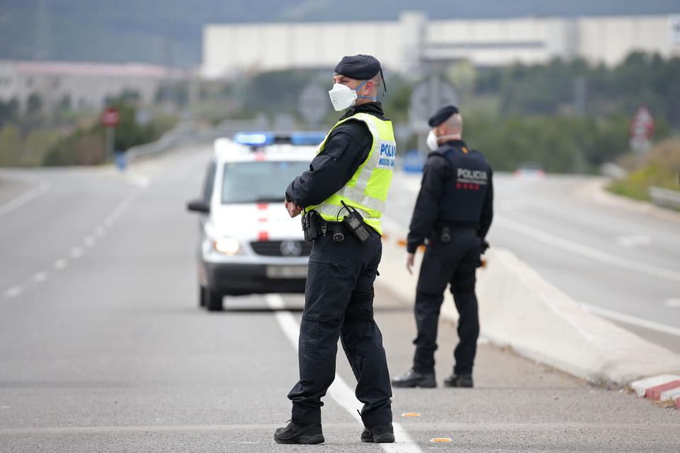 Police officers stand on the closed off road near Igualada, Spain, Friday, March 13, 2020. Over 60,000 people awoke Friday in four towns near Barcelona confined to their homes and with police blocking roads. The order by regional authorities in Catalonia is Spain's first mandatory lockdown as COVID-19 coronavirus infections increase sharply, putting a strain on health services and pressure on the government for more action. For most people, the new coronavirus causes only mild or moderate symptoms, such as fever and cough. For some, especially older adults and people with existing health problems, it can cause more severe illness, including pneumonia. (AP Photo/Joan Mateu)