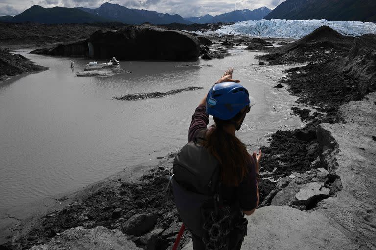 Un guía turístico señala el glaciar Matanuska desde una cornisa inestable sobre un estanque formado por el retroceso del glaciar