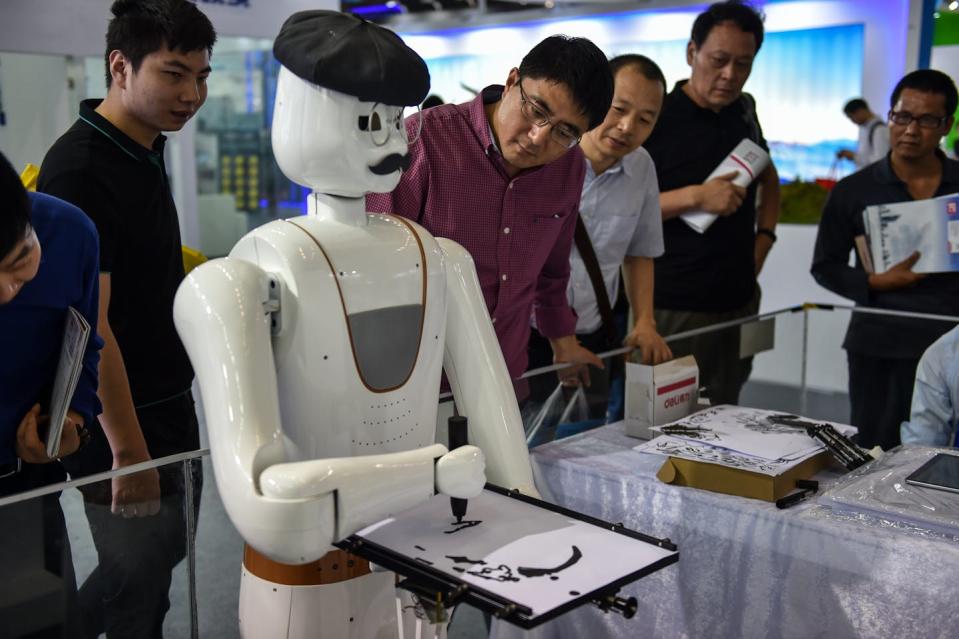 A robot paints while people watch.