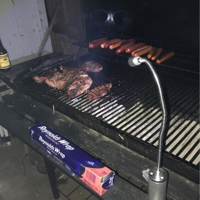 Barbecue grill with steaks and hot dogs cooking, a box of Reynolds Wrap, and a grill light attached for visibility