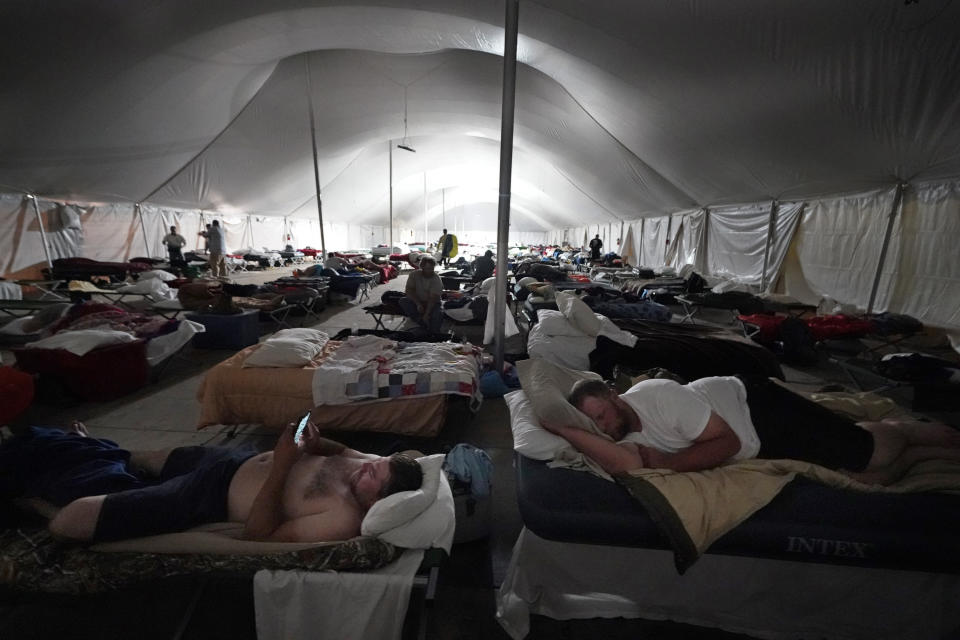 Workers bunk down for the night in a tent city for electrical workers in Amelia, La., Thursday, Sept. 16, 2021. In one massive white tent, hundreds of cots are spread out; experienced workers bring their own inflatable mattresses. Another tent houses a cafeteria that serves hot breakfast starting about 5 a.m., dinner and boxed lunches that can be eaten out in the field. (AP Photo/Gerald Herbert)