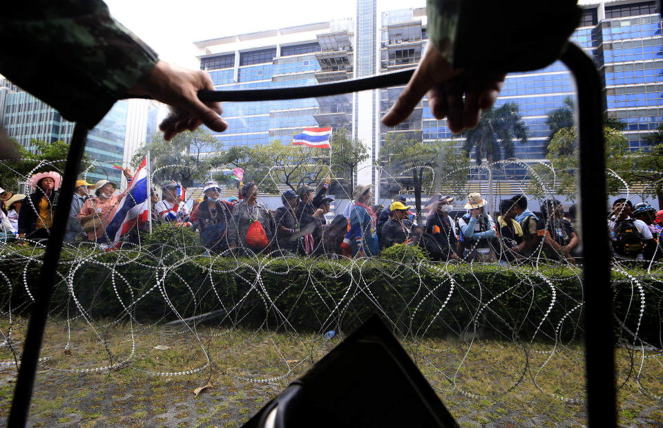 A Thai soldier, foreground, looks at anti-government protesters led by Suthep Thaugsuban stage a rally outside the office of Permanent Secretary for Defense, a temporary office of Prime Minister Yingluck Shinawatra on the outskirts of Bangkok, Thailand Wednesday, Feb. 19, 2014. Anti-government protesters surrounded Yingluck's temporary office in Bangkok's northern outskirts to demand her resignation a day after clashes with police. (AP Photo/Wason Wanichakorn)