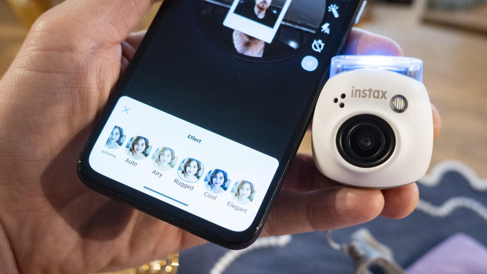 White Fujifilm Instax Pal alongside smartphone with Instax Pal app on the display