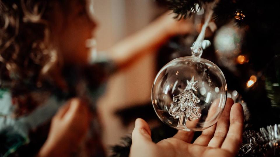 Little girl admires the tree ornaments with Mom