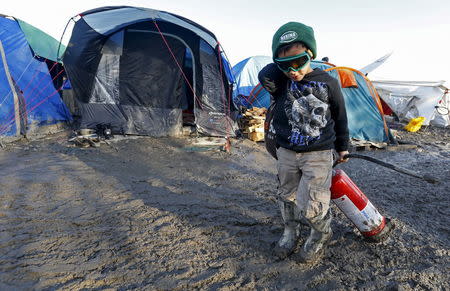 A young migrant pulls a fire extinguisher in a muddy field at a camp of makeshift shelters for migrants and asylum-seekers from Iraq, Kurdistan, Iran and Syria, called the Grande Synthe jungle, near Dunkirk, France, January 25, 2016. REUTERS/Yves Herman