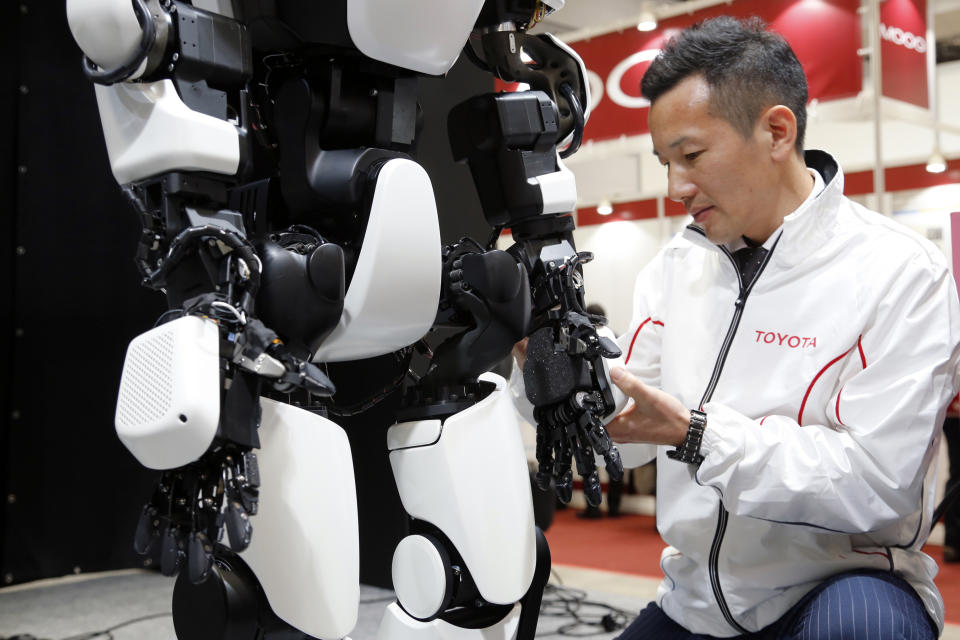 In this Dec. 18, 2019, photo, Toyota Motor Corp. engineer Tomohisa Moridaira, shows a upgraded version of the human-shaped T-HR3, which now has enhanced finger movements that can be remotely controlled during a demonstration in Tokyo. In the demonstration, a person wearing a headset and wiring made the robot move in exactly the same way he was moving, waving or making dance-like movements, as sensors sent computerized signals to the robot of what they detected as human movements. (AP Photo/Yuri Kageyama)