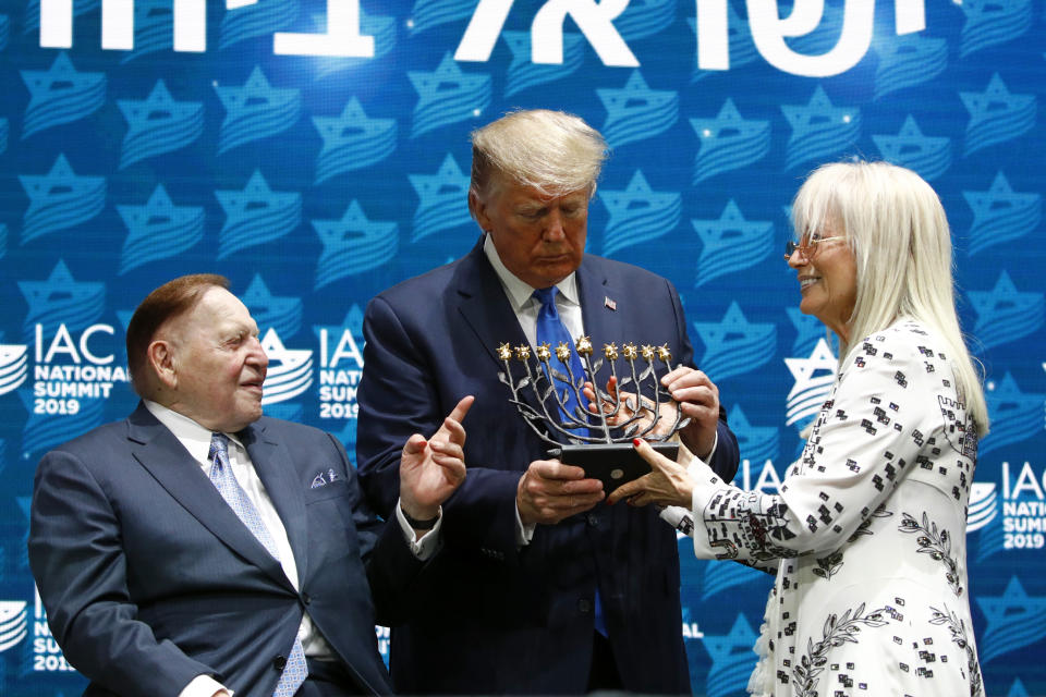 President Donald Trump receives a menorah from Las Vegas Sands Corporation Chief Executive and Republican mega donor Sheldon Adelson, left, and his wife Miriam Adelson at the Israeli American Council National Summit in Hollywood, Fla., Saturday, Dec. 7, 2019. (AP Photo/Patrick Semansky)