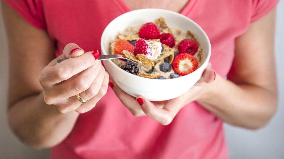 close up crop of woman holding a bowl containing homemade granola or muesli with oat flakes, corn flakes, dried fruits with fresh berries healthy breakfast