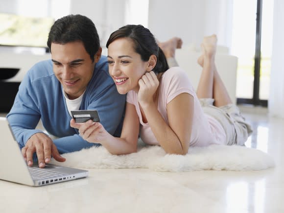 Barefoot couple lying on floor at home shopping on a laptop with credit card.