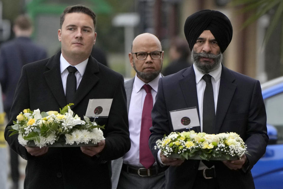 British lawmakers Wes Streeting, left and Jas Athwal, right, leader of Redbridge Council, carry floral tributes to be laid near the Belfairs Methodist Church where British lawmaker David Amess was killed Friday during a meeting with constituents, in Leigh-on-Sea, Essex, England, Sunday, Oct. 17, 2021. Amess, a long-serving lawmaker, was attacked during a regular meeting with his constituents at a church in Leigh-on-Sea, a town about 40 miles (62 kilometers) east of London. (AP Photo/Alastair Grant)