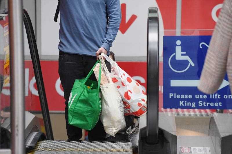 A man carries reusable Coles bags up an escalator in Sydney.