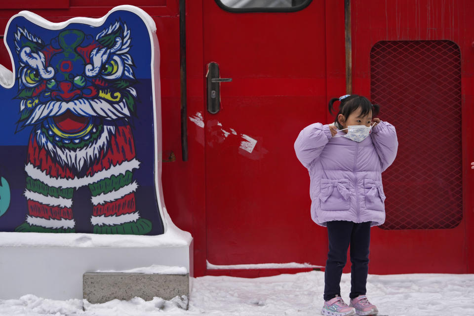 A child puts on her face mask to help protect from the coronavirus next to a lion dancer decoration at a mall in Beijing, Sunday, Jan. 23, 2022. Chinese authorities have called on the public to stay where they are during the Lunar New Year instead of traveling to their hometowns for the year's most important family holiday. (AP Photo/Andy Wong)