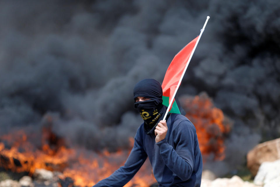 Protester holding a Palestinian flag runs through burning tires