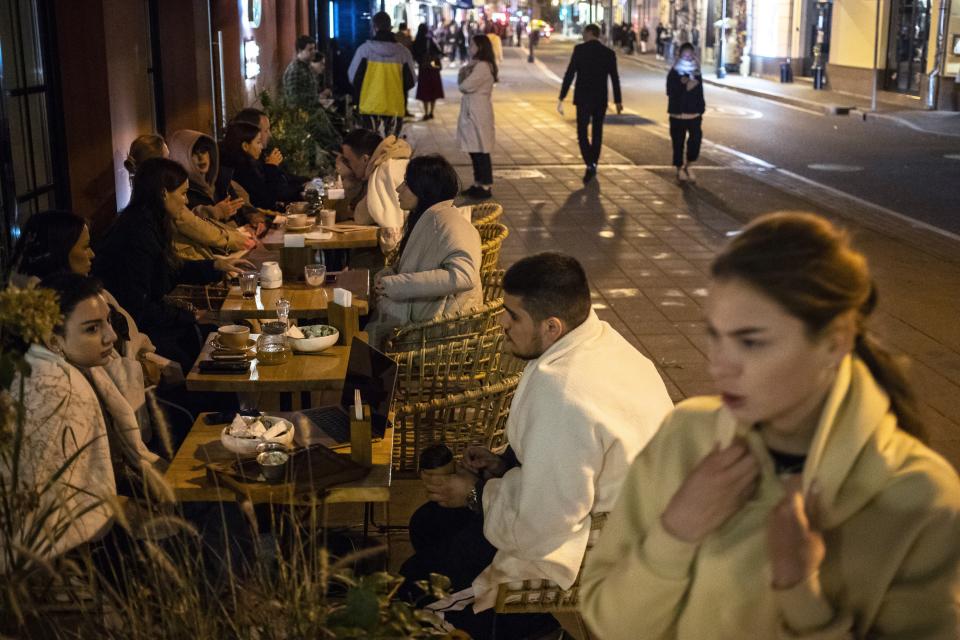 Customers sit outside a restaurant at Patriarshiye Prudy, a hip restaurant and bar district in Moscow, Russia, late Friday, Oct. 16, 2020. The outbreak in Russia this month is breaking the records set in the spring, when a lockdown to slow the spread was put in place. But, as governments across Europe move to reimpose restrictions to counter rising cases, authorities in Russia are resisting shutting down businesses again. (AP Photo/Pavel Golovkin)