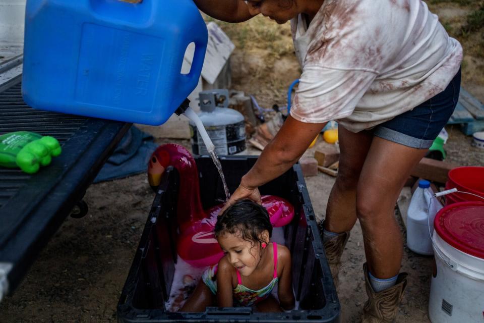 A mother pours water on her daughter's head to wash her hair.