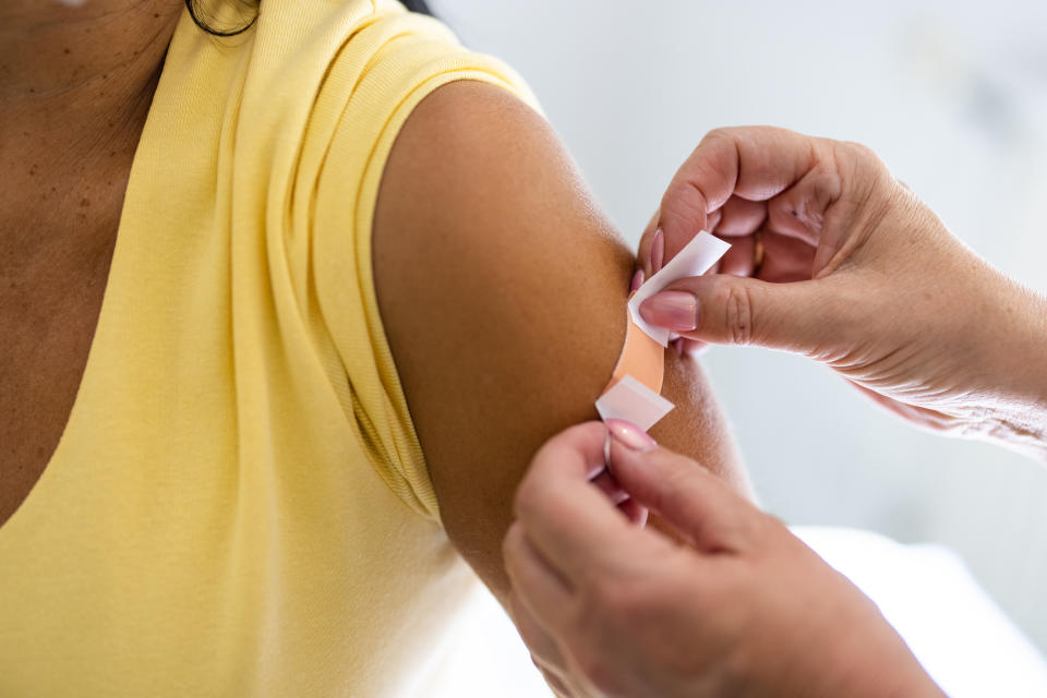 Close-up of a female doctor putting a band-aid on the arm of a woman after giving vaccine injection in the clinic. Healthcare professional hands placing a bandage on a female's arm after covid-19 vaccination.