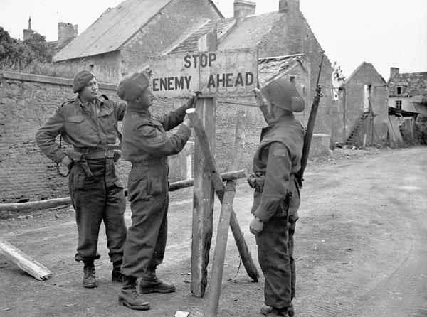 <p>Photographer: Dubervill, Frank L. Location: Bretteville-le-Rabet, France. Description: Sgt. T.S. Giles (Winnipeg, Man.) (centre) and Lt. Howard Germen (Drumheller, Alta.) (holding sign in place). Credit: Library and Archives Canada</p> 