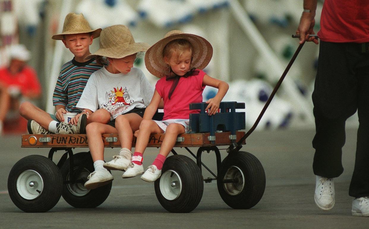 Hats for protection from the sun and a ride in a wagon are the best ways to be comfortable on a hot day at the Ohio State Fair in 1995. The Ziegenhardt children from Mason, Ohio, had their dad Frank provide the towing as they went from one fair attraction to another. From left are Zachary, 8; Iris, 6; and Hannah Ziegenhardt, 4.