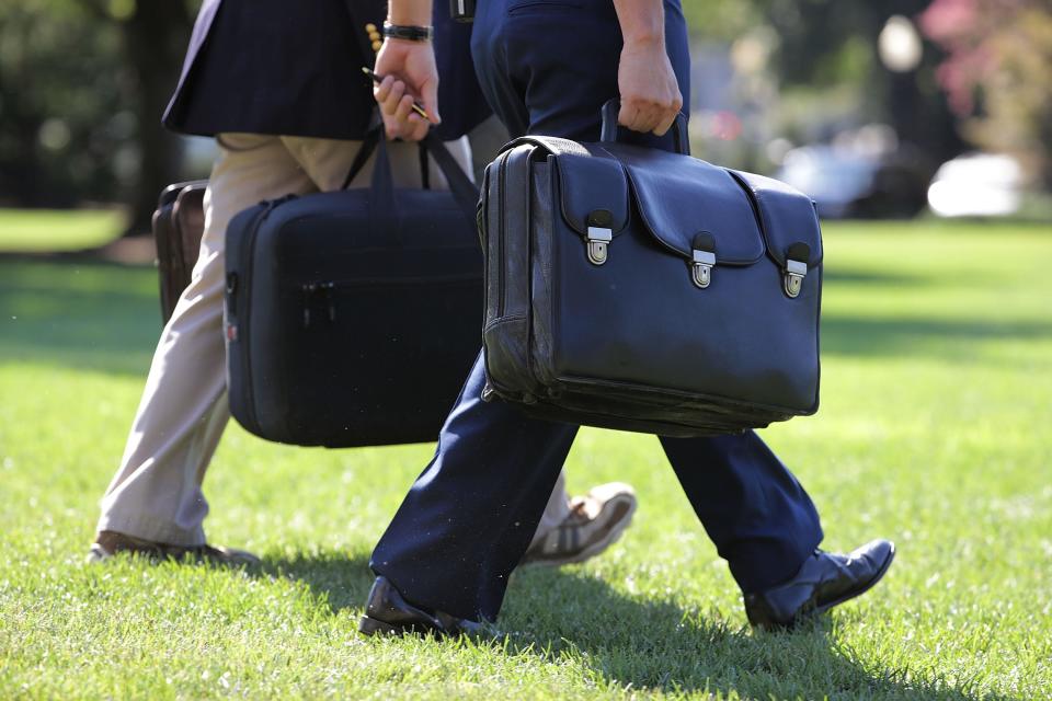 A military aide carries the "football," a case with he launch codes for nuclear weapons, as he follows President Obama across the South Lawn of the White House before boarding Marine One Aug.  23, 2016