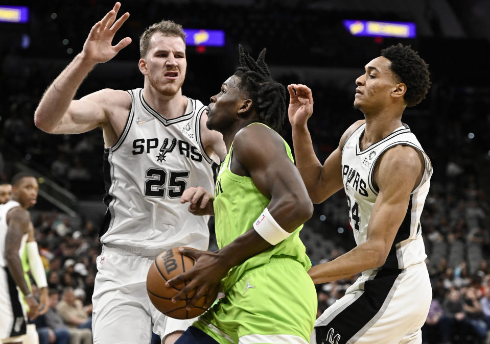 Minnesota Timberwolves' Anthony Edwards, center, drives against San Antonio Spurs' Jakob Poeltl (25) and Devin Vassell during the first half of an NBA basketball game on Monday, March 14, 2022, in San Antonio. (AP Photo/Darren Abate)