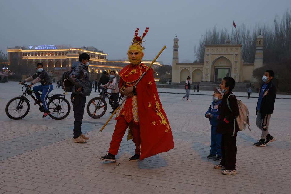 A performer dressed as the monkey god from a Chinese fable walks near a mosque as Uyghur children gaze upon him Kashgar in northwestern China's Xinjiang Uyghur Autonomous Region on Friday, March 19, 2021. Four years after Beijing's brutal crackdown on largely Muslim minorities native to Xinjiang, Chinese authorities are dialing back the region's high-tech police state and stepping up tourism. But even as a sense of normality returns, fear remains, hidden but pervasive. (AP Photo/Ng Han Guan)