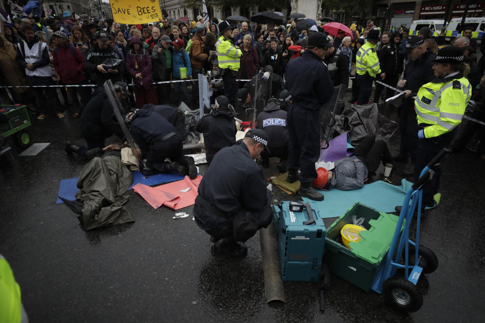 Police officers cut apart a pipe helping Extinction Rebellion climate change protesters stay locked together as they lie down blocking a road at the bottom of Trafalgar Square in London, Friday, Oct. 11, 2019. Some hundreds of climate change activists are in London during a fifth day of protests by the Extinction Rebellion movement to demand more urgent actions to counter global warming. (AP Photo/Matt Dunham)