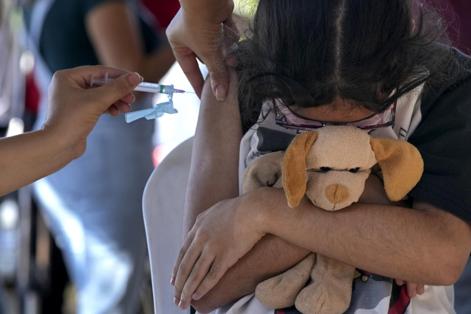 A girl hugs her stuffed toy as she gets a shot of the Pfizer COVID-19 vaccine at a community health center, in Brasilia, Brazil, Sunday, Jan. 16, 2022. Brasilia started the COVID-19 vaccination of children between ages 5 and 11. (AP Photo/Eraldo Peres)