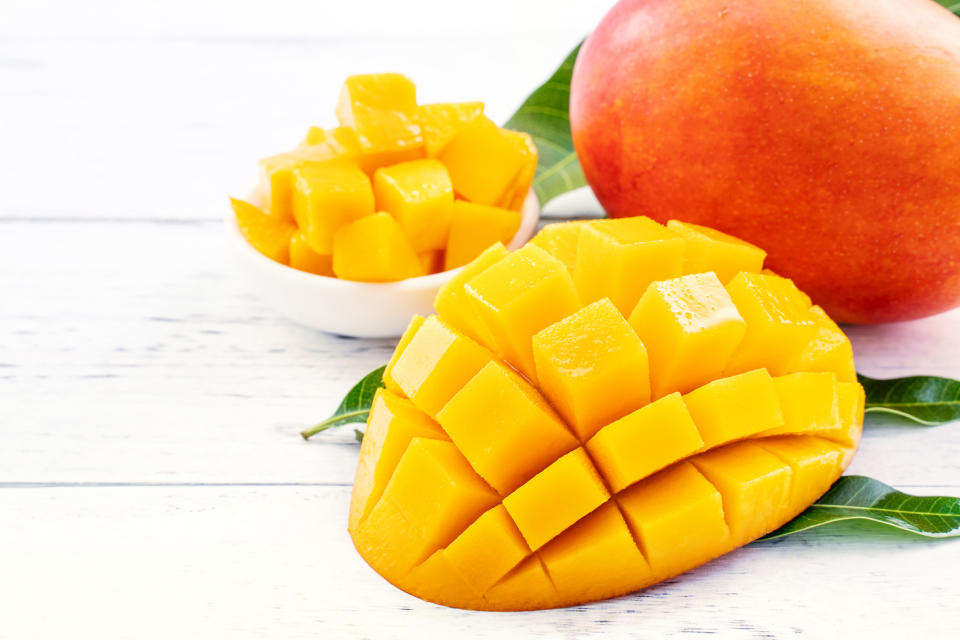 Beautiful chopped mango with green leaves on bright white color timber background. Above Top view, flat lay, copy space, close up. Tropical fruit concept.