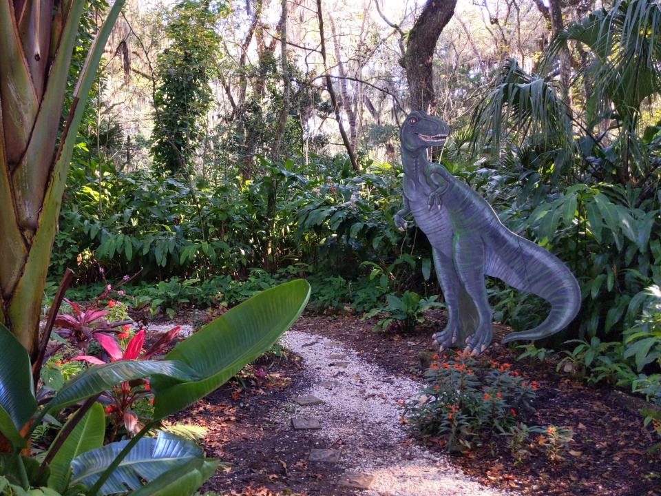A garden with trees, flowers, and a dinosaur statue.