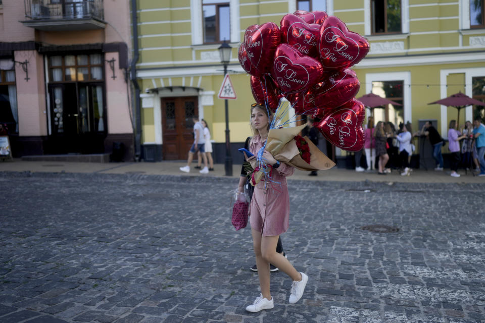 A woman crosses a street with balloons in Kyiv, Ukraine, Wednesday, June 1, 2022. (AP Photo/Natacha Pisarenko)