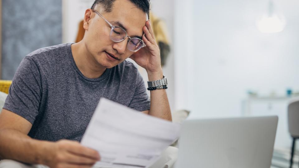 Sad man looking at his monthly bills at home.