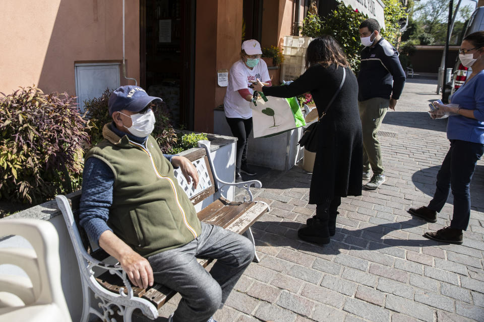 In this photo taken on Friday, April 10, 2020 nurse Cristina Settembrese receives food to be shared with colleagues from her mother Filomena as her father Palmiro looks on at left outside their bakery in Basiglio, Italy. Settembrese spends her days caring for COVID-19 patients in a hospital ward, and when she goes home, her personal isolation begins by her own choice. (AP Photo/Luca Bruno)