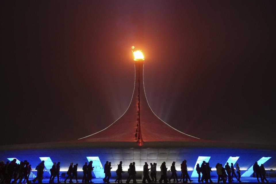 Spectators walk past the Olympic flame on a foggy night in Olympic Park during the 2014 Winter Olympics on Sunday, Feb. 16, 2014, in Sochi, Russia. (AP Photo/J. David Ake)